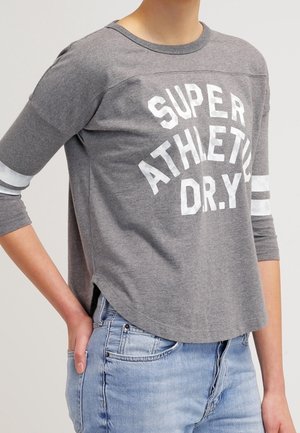 T-shirt gris à manches longues avec imprimé blanc "SUPER ATHLETIC D.R.Y.", ourlet arrondi et rayures blanches sur les manches. Fabriqué en tissu doux en mélange de coton.