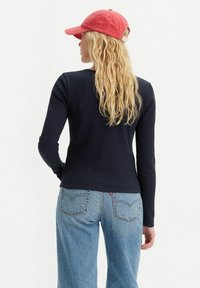 Haut bleu marine à manches longues côtelé, coupe ajustée, associé à un jean bleu clair à jambes droites avec poches arrière et détails de surpiqûres subtils.