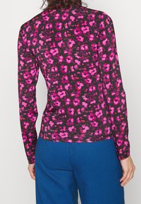 Camicia a maniche lunghe in tessuto trasparente nero con un motivo floreale rosa, abbinata a pantaloni a quadri blu. Il design è aderente e leggero.