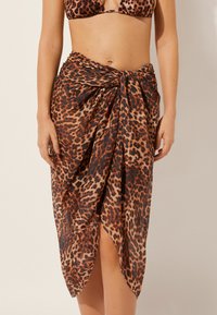 Sarong de estampado de leopardo en tela ligera y transparente, con detalle anudado en la cintura y una abertura alta para estilo y comodidad al llevarlo.
