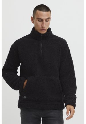 Pull noir en polaire avec un col haut, fermeture éclair quart et poche avant. Extérieur doux et texturé avec une coupe décontractée.
