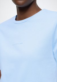 Ανοιχτό μπλε μπλουζάκι από απαλό βαμβάκι με στρογγυλή λαιμόκοψη. Διαθέτει ένα τυπωμένο λογότυπο σε διακριτικό τόνο στο στήθος. Απλός σχεδιασμός, κοντά μανίκια.