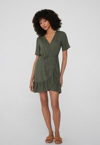 Robe portefeuille vert olive avec des manches courtes, décolleté en V, taille à nouer et ourlet volanté. Texture lisse, design décontracté. Inclut des sandales à talons plissées marron.