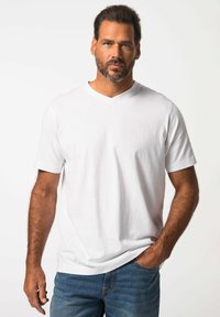 Camiseta blanca de cuello en V en tejido suave, de mangas cortas, con un sutil logo en el lado izquierdo del pecho, combinada con jeans de mezclilla azules.