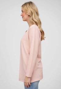 Roze langemouwen top met een relaxte pasvorm, voorzien van een ronde halslijn en subtiele horizontale strepen, gecombineerd met lichtblauwe spijkerbroek.