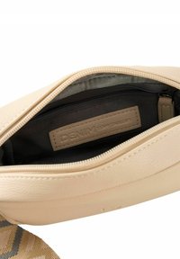 Borsa a mano beige chiaro in materiale sintetico testurizzato. Presenta una fodera interna nera e una tasca con zip. Etichetta del marchio visibile all'interno.