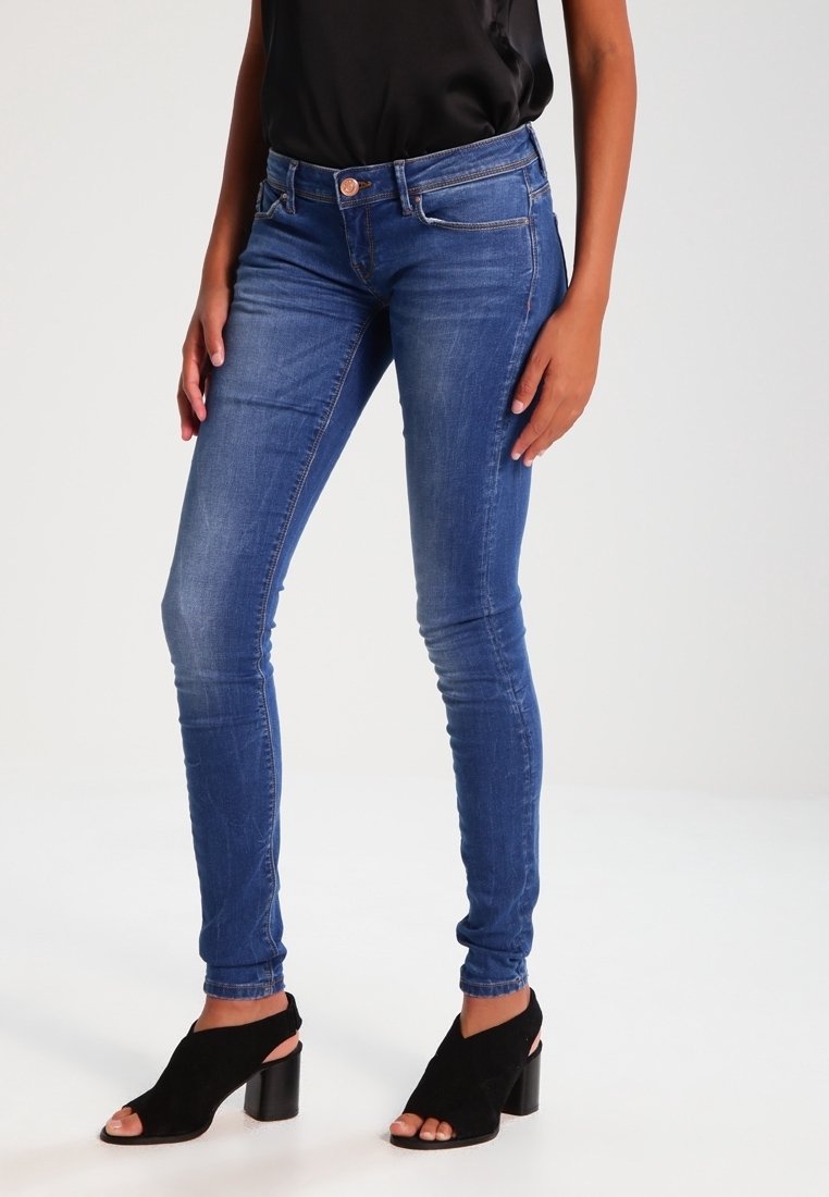 Vaqueros ajustados de mezclilla azul con una textura suave, que cuentan con cinco bolsillos, cierre de botón y un corte slim. Combinados con zapatos de tacón alto negros.