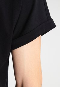 Camiseta de algodón negra con un dobladillo de manga doblado, que presenta una textura suave y una vista en primer plano de la manga y el brazo.