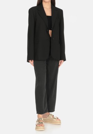 Blazer oversize nero con scollo a revers, abbinato a un top nero corto, jeans neri a gamba larga e sandali con piattaforma beige con dettagli.