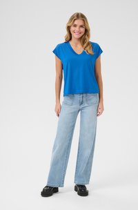 Blue short-sleeve V-neck top paired with light blue wide-leg jeans and black platform shoes. Smooth fabric with a relaxed fit.