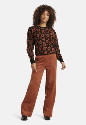Pull noir avec un imprimé léopard rouille, associé à un pantalon large de couleur rouille. Le pull possède des manches bouffantes et des poignets côtelés.