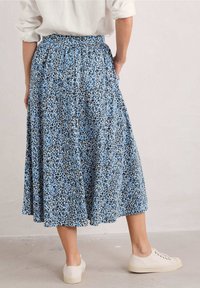 Sininen ja musta kukkakuosiset hame, jossa on joustava vyötärö, virtaava kangas ja sivutaskut. Yhdistetty valkoisiin lenkkareihin.