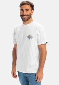 Hvid bomulds t-shirt med korte ærmer, prydet med et diamantformet grafisk design i blå og orange. Designet til en afslappet pasform.
