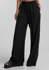 Pantaloni neri a gamba larga realizzati in tessuto morbido con vita elastica, dotati di tasche laterali e una vestibilità morbida per il massimo comfort.