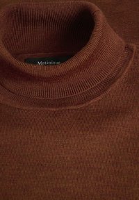 Brūns turtlenecks džemperis izgatavots no ribota auduma. Ir augsta apkakle un smalka tekstūra. Etiķetē rakstīts "Matinique."