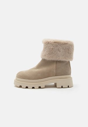 Stivaletto beige in suede con suola spessa in gomma e polsino morbido in pelliccia sintetica piegato attorno alla parte superiore.