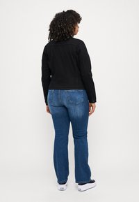 Black denim jacket, fitted design, button-up closure; blue flared jeans, textured fabric, back pockets; white sneakers with black accents.