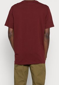 T-shirt di cotone color bordeaux con maniche corte e scollatura a girocollo. Texture liscia, vestibilità comoda e nessun logo o motivo visibile.