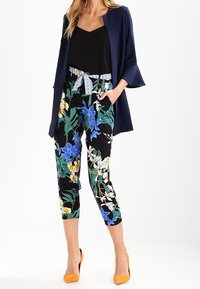 Marinblazer med trumpetärmar, svart topp och blommönstrade cropped-byxor i blått, grönt och gult. Bärs med gula klackar.