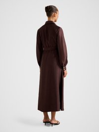 Brünett pikkade varrukatega kleit tumepruunist kangast, vöökohast kokku tõmmatud ja nööbitavate mansettidega. Keskmise pikkusega, sirge lõikega ja külje lõhikuga.