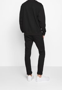 Felpa nera e pantaloni attillati. La felpa ha un colletto rotondo. Sneakers bianche offrono un contrasto all'outfit interamente nero.