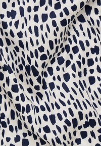 Tissu blanc avec des taches noires irrégulières ressemblant à un imprimé dalmatien, montrant des plis et une texture visibles.