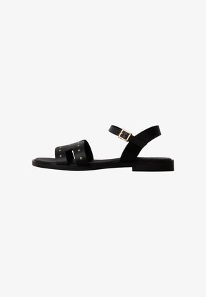 Black flat sandal with an ankle strap, gold buckle, and two front straps featuring small gold studs.