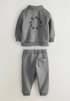 Hall hallitamisülikond, millel on kraega jakk musta graafilise trükiga ja sobivad dressipüksid küljetaskuga. Pehme, tekstureeritud kangas.