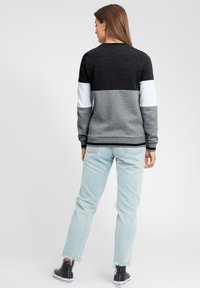 Grå og svart fargeblokkert sweatshirt med rund hals; kombinert med lyseblå slitte jeans og svarte høye sneakers.