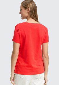 Rode T-shirt met korte mouwen, ronde halslijn en een losse pasvorm; gladde textuur; label aan de zoom; gezien vanuit de achterkant tegen een lichte achtergrond.