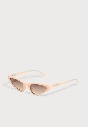 Lunettes de soleil œil de chat avec montures beige clair et verres marron dégradés posées sur une surface blanche.
