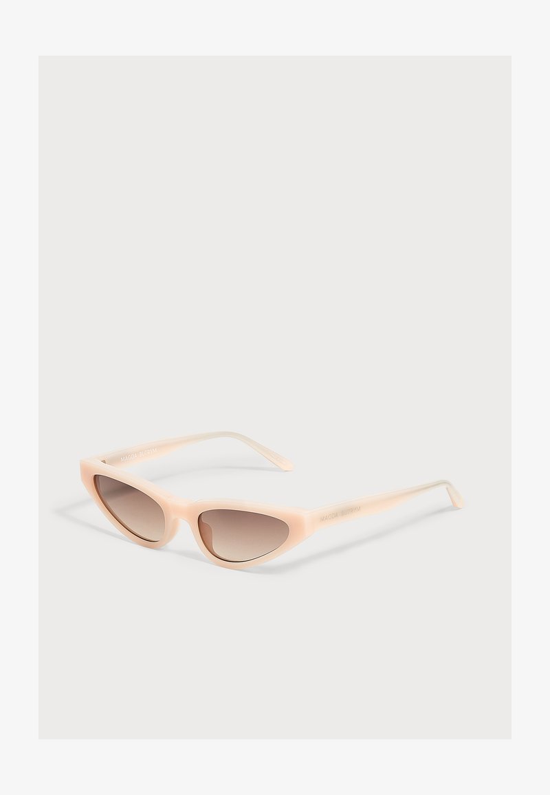 Lunettes de soleil œil de chat avec montures beige clair et verres marron dégradés posées sur une surface blanche.