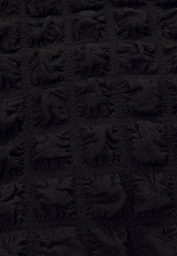 Tessuto nero lavorato a maglia con un motivo testurizzato caratterizzato da rilievi a forma di leone, disposto a griglia, che offre un aspetto morbido e denso.