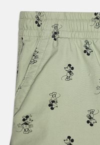 Shorts verts clairs en tissu doux, ornés d'un motif répétitif noir de Mickey Mouse et avec une taille élastique.