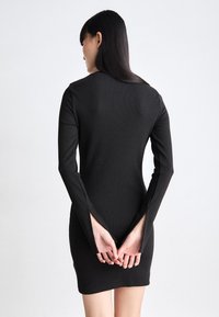 Black ribbed long-sleeve dress with a fitted silhouette. Features split sleeves and a round neckline, showcasing a sleek design.
