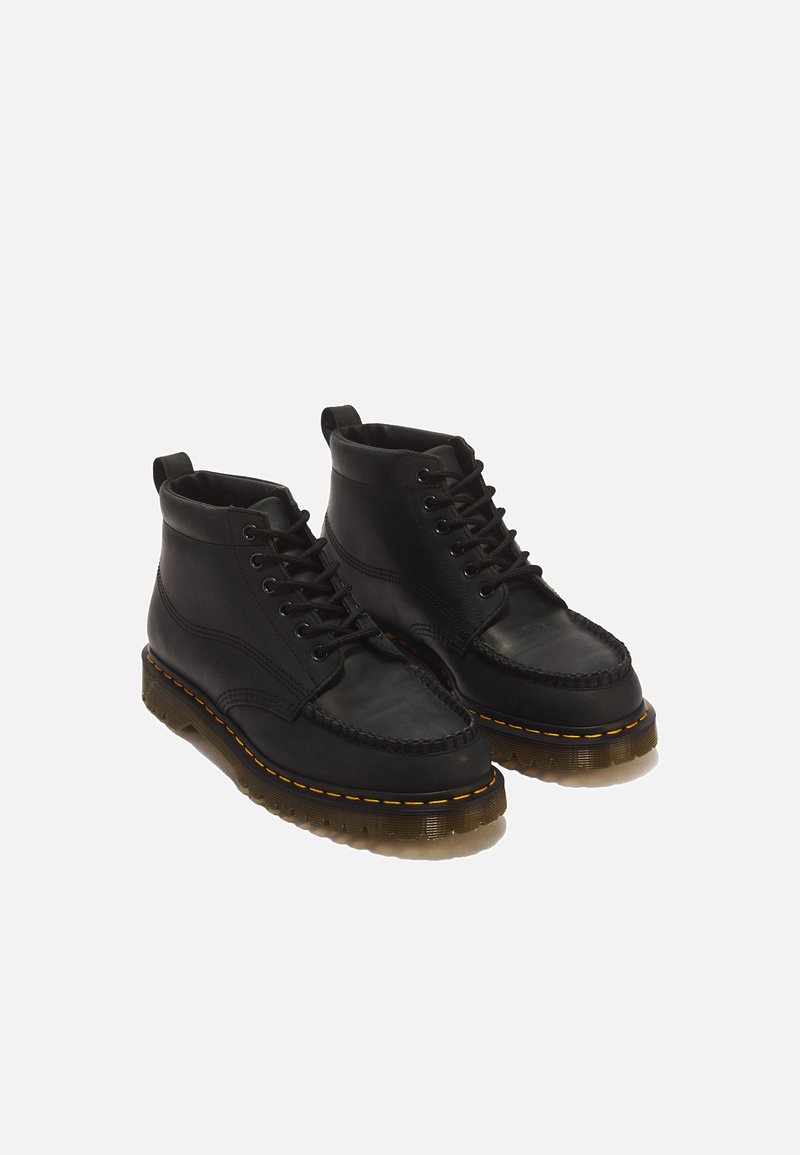 Ein Paar schwarze Leder-Schnürstiefeletten mit dicken durchsichtigen Sohlen und gelber Naht um die Sohlen.
