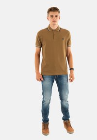 Bruine polo met een witte en zwarte kraagafwerking, gecombineerd met lichtblauwe jeans en bruine veterschoenen. Casual fit, korte mouwen.