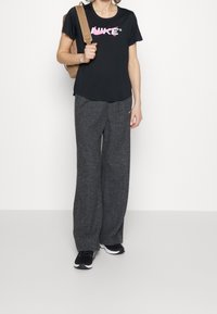 Camiseta negra de manga corta con el logo rosa de Nike, combinada con pantalones de chándal anchos de color gris oscuro y zapatillas deportivas negras. Mochila beige sobre el hombro.