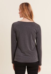 Langärmliges graues T-Shirt mit rundem Halsausschnitt, weicher Textur und abgerundetem Saum, kombiniert mit schwarzen Hosen. Einfaches und geradliniges Design.