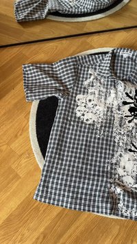 Camicia a maniche corte a quadri bianco e nero con una stampa grafica che presenta teschi e schizzi su un lato. Tessuto in cotone, vestibilità ampia.