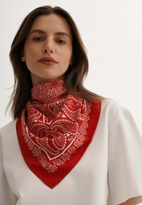 Czerwona bandana w kwiatowy wzór z białymi paisley, wykonana z gładkiego materiału, zawiązana wokół szyi; kwadratowy kształt z ostrymi końcami.