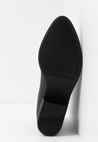 Semelle de chaussure en cuir noir avec une surface lisse, un dessous en caoutchouc texturé et un talon effilé. Présente un indicateur de taille en relief "37".