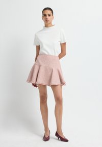 Witte top met korte mouwen, gecombineerd met een roze tweed fluïde rok met een rafelige zoom, gedragen met paarse hoge hakken. Eenvoudig, gestructureerd ontwerp.