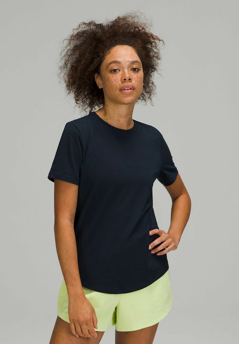 Marineblauwe t-shirt met korte mouwen van gladde stof. Voorzien van een ronde halslijn en een ontspannen pasvorm, gecombineerd met lichtgroene shorts.