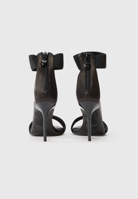 Μαύρα ψηλά τακούνια με σατινέ φινίρισμα, ανοιχτή μύτη, φερμουάρ στο πίσω μέρος και μαλακές ελαστικές λωρίδες γύρω από τον αστράγαλο.