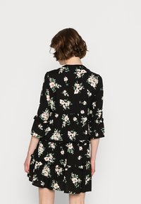 Vestido preto floral feito de um tecido leve, apresentando mangas de sino de três quartos, camadas com babados e pequenos padrões de flores brancas e cor-de-rosa.