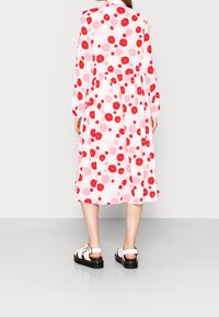 Abito a maniche lunghe, lunghezza ginocchio, con tessuto bianco decorato da motivi floreali rossi e rosa, vita arricciata e gonna fluida.