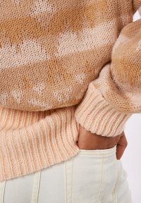 Suéter de punto con rayas beige y marrón claro. Puños y dobladillo acanalados, textura suave. Combinado con pantalones ajustados de color claro.