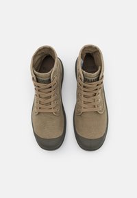 Botas de tobillo de lona color tostado con una punta de goma oscura. Presentan cordones beige y una marca en la lengüeta, con una textura suave en toda su superficie.