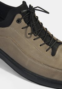 Baskets en cuir marron avec des accents noirs, surface texturée, lacets noirs et coutures contrastées. Dotées d'une semelle en caoutchouc pour la durabilité.